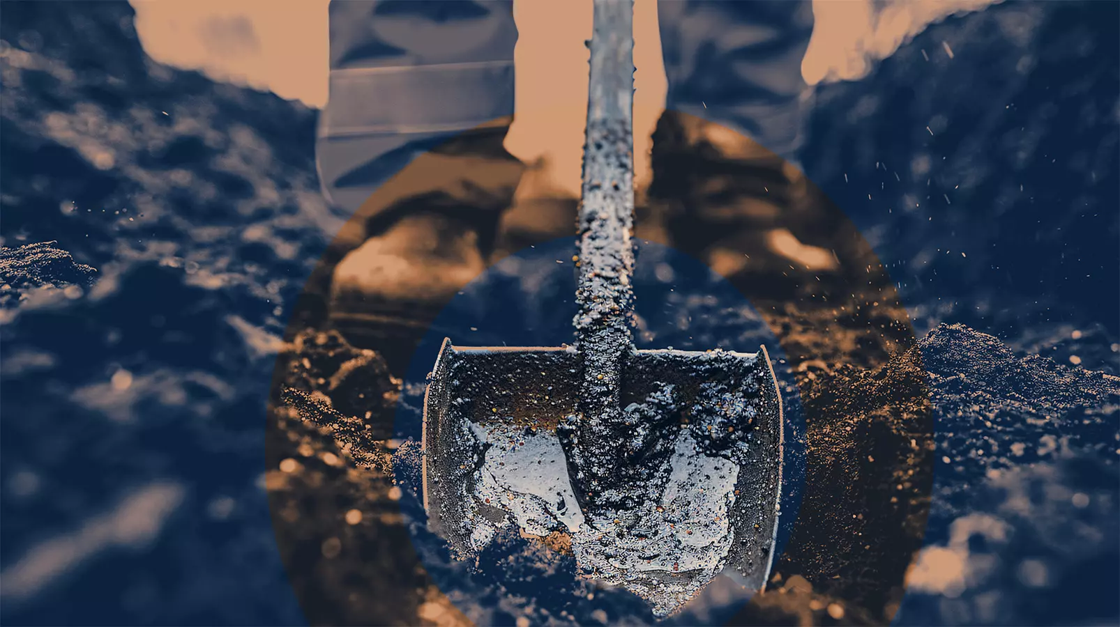 Close-up of a shovel digging into soil with a worker standing behind, highlighting manual groundwork.