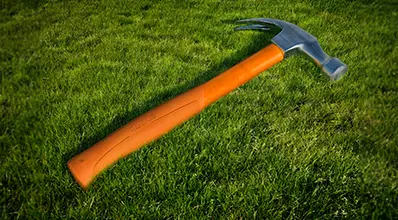 alt="Orange claw hammer on the grass."