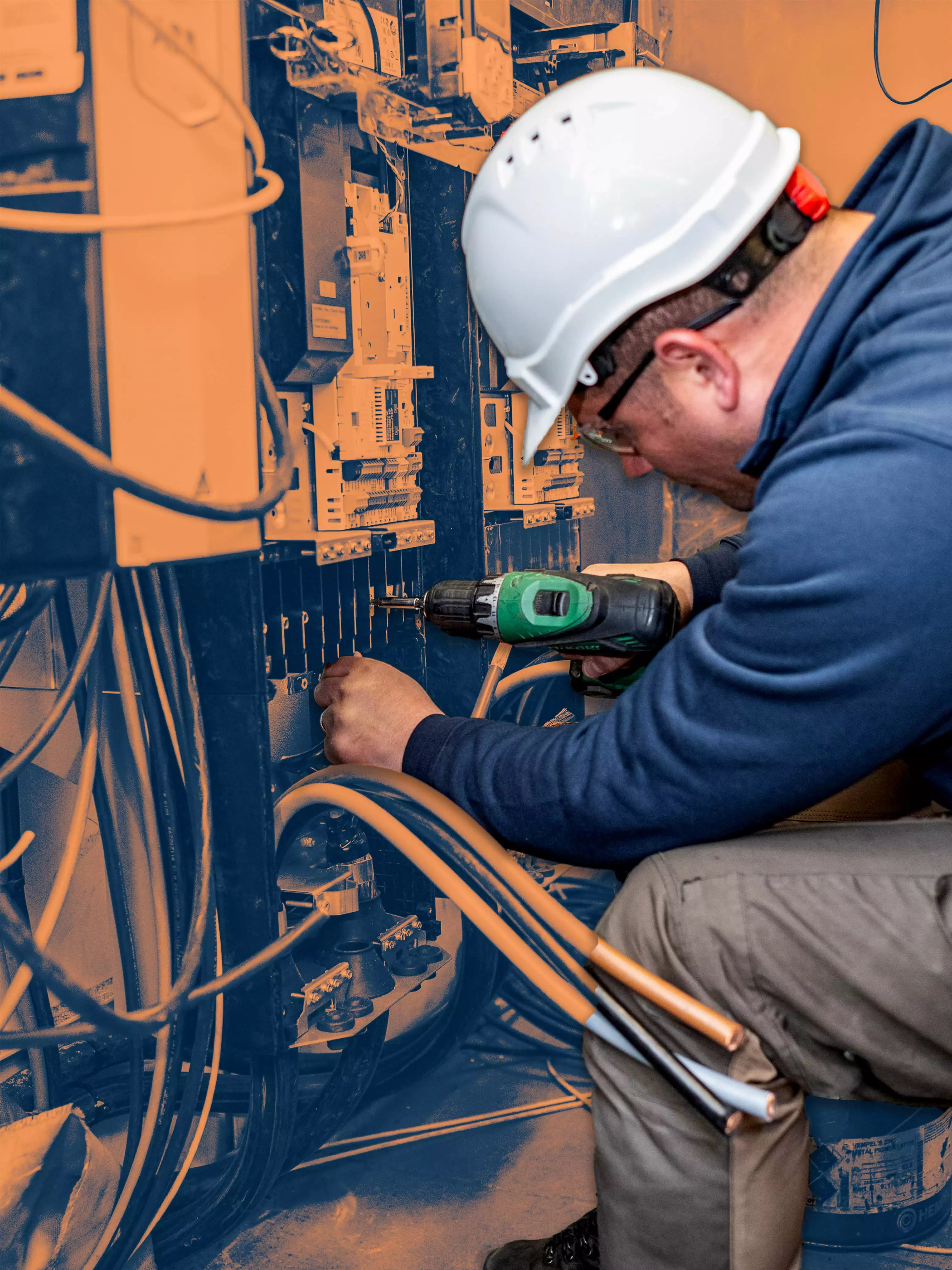 E&I worker in a white helmet using a drill to work on an electrical cabinet.