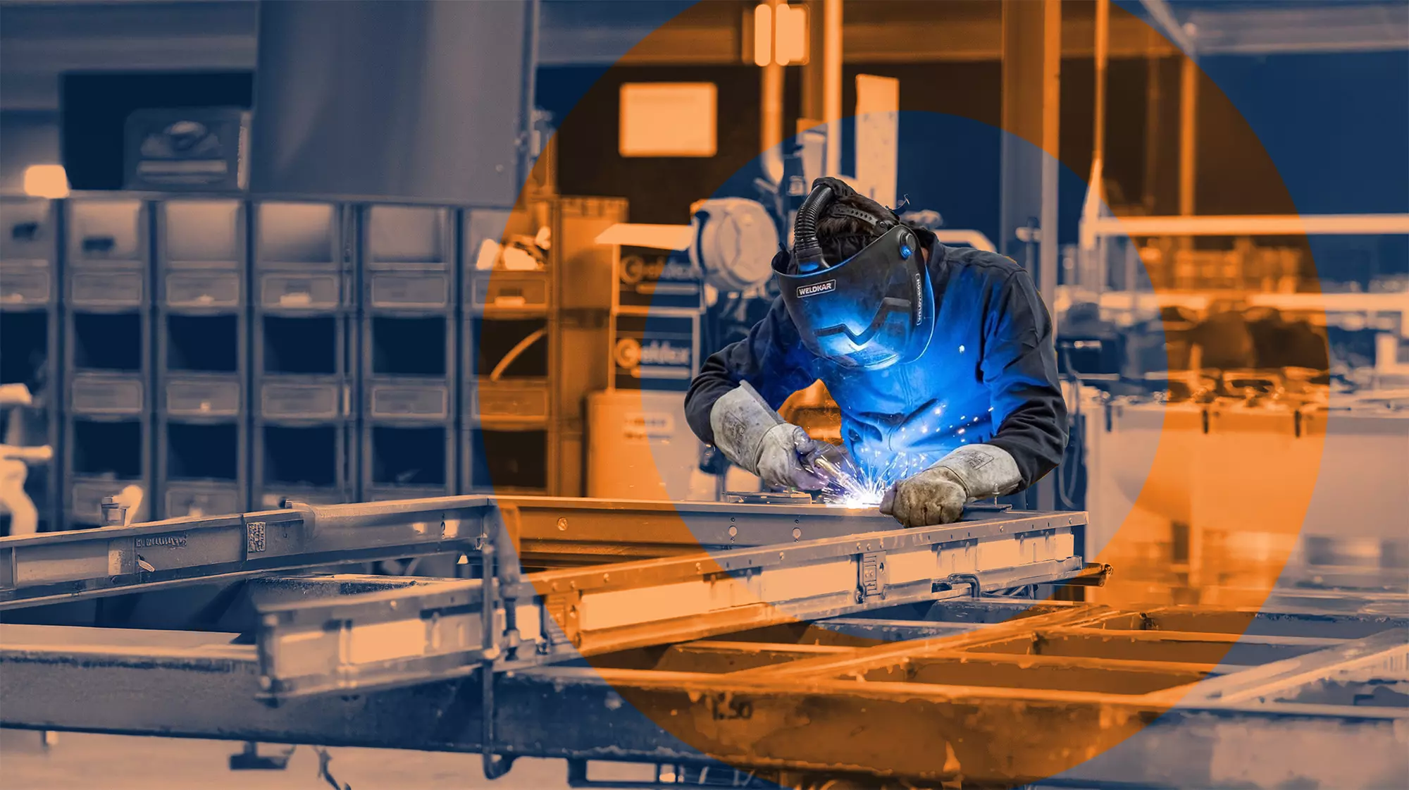 Welder wearing protective gear working on a metal frame in a workshop, producing visible sparks.