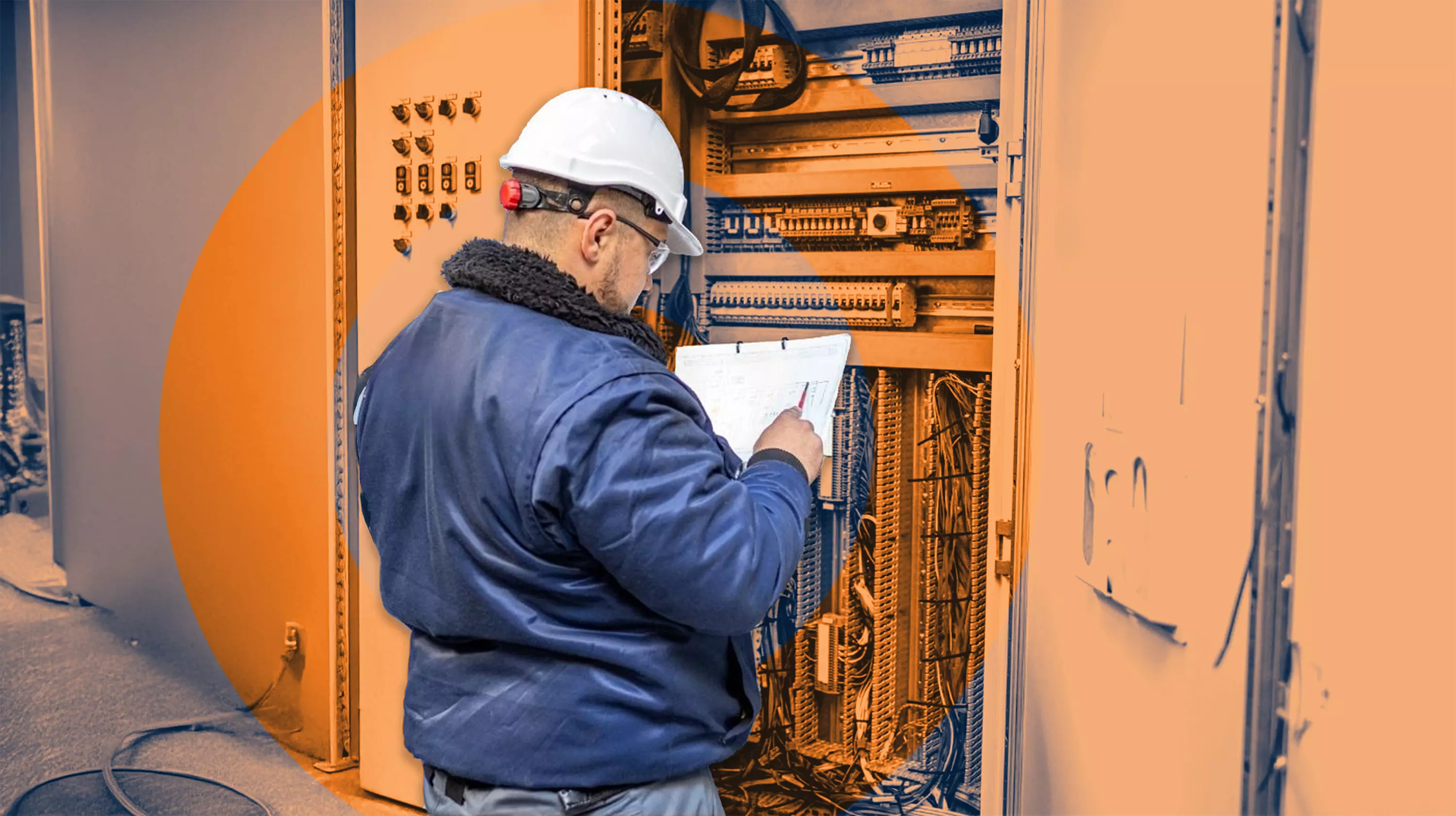 Construction worker inspecting and checking wiring plans at an open electrical control cabinet.