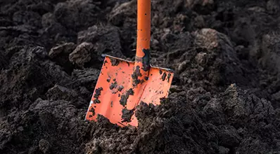 alt="Orange shovel stuck in soil, representing infra work."