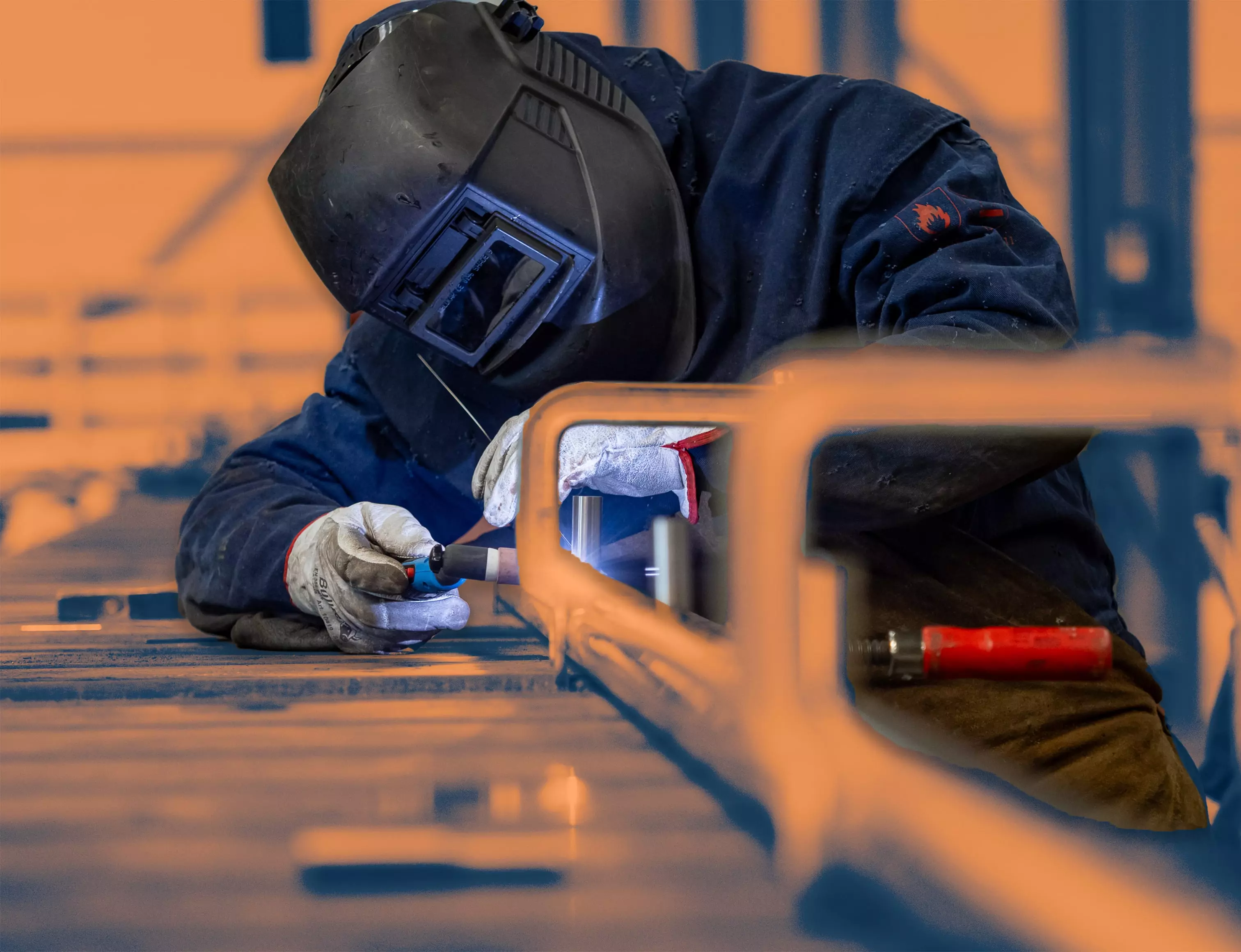 Close-up of a welder performing TIG welding on a metal structure, wearing gloves and a helmet.
